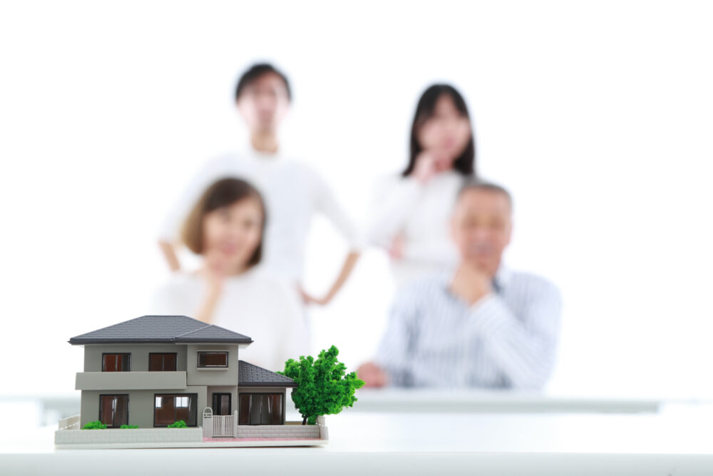 家の模型を前に置いて考える4人の家族 住宅ローン資金援助 贈与税非課税特例
